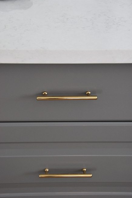 installing gold cabinetry hardware in a grey and white kitchen - via the sweetest digs
