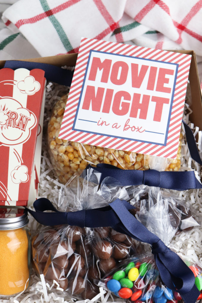 Movie night in a box filled with a popcorn bag, seasoning salt, kernals and candy.