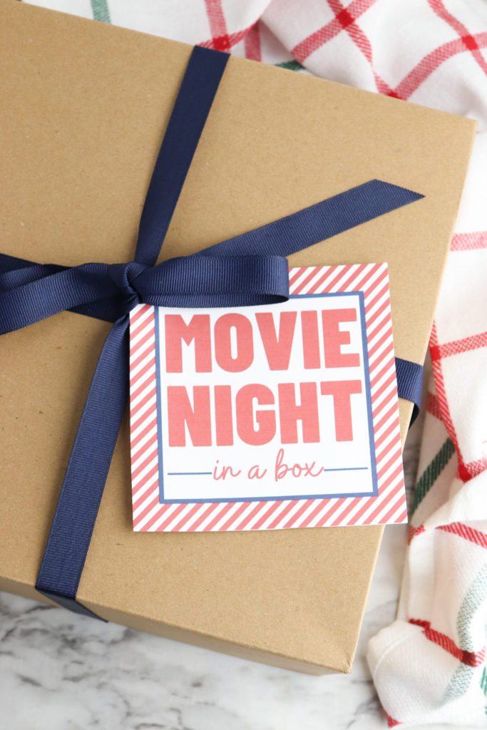 Cardboard box wrapped with ribbon and a movie night printable gift tag.